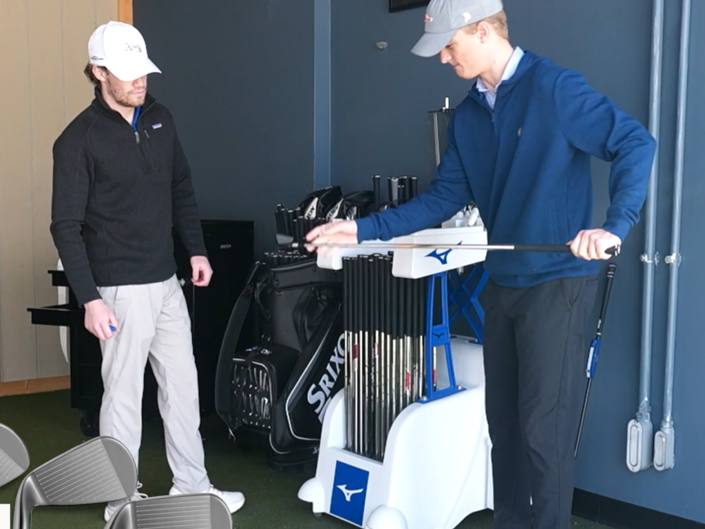 club fitter talking to customer about golf clubs with fitting carts in background